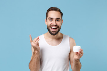 Bearded young man 20s years old applying moisturizer facial cream from container isolated on blue pastel background studio portrait. Skin care healthcare cosmetic procedures concept Mock up copy space