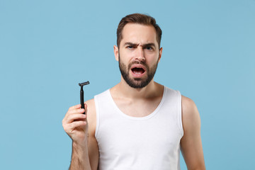 Bearded man 20s years old in white shirt hold one-off disposable plastic razor isolated on blue...