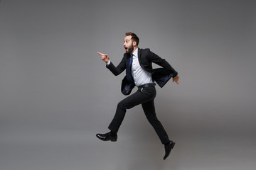 Side view of excited young business man in classic suit shirt tie posing isolated on grey background. Achievement career wealth business concept. Mock up copy space. Jumping, point index finger aside.