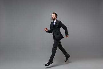 Fototapeta na wymiar Side view of cheerful young business man in classic suit shirt tie posing isolated on grey background. Achievement career wealth business concept. Mock up copy space. Running, jumping, looking aside.