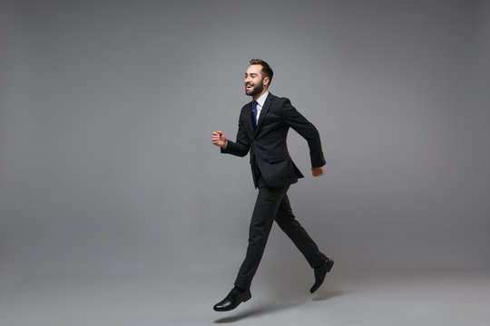 Side view of cheerful young business man in classic suit shirt tie posing isolated on grey background. Achievement career wealth business concept. Mock up copy space. Running, jumping, looking aside.