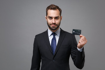 Handsome young business man in classic black suit shirt tie posing isolated on grey wall background in studio. Achievement career wealth business concept. Mock up copy space. Holding credit bank card.