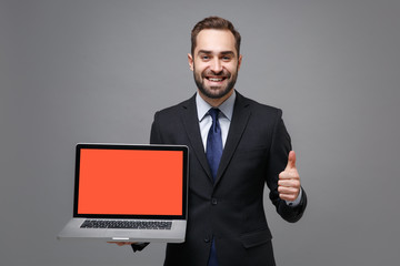 Young business man in suit shirt tie posing isolated on grey background. Achievement career wealth business concept. Mock up copy space. Hold laptop computer with blank empty screen showing thumb up.