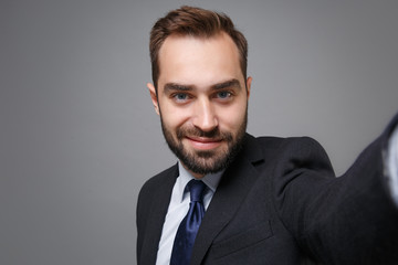Close up of handsome young business man in classic suit shirt tie posing isolated on grey background. Achievement career wealth business concept. Mock up copy space. Doing selfie shot on mobile phone.