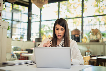 Beautiful caucasian elegant businesswoman sitting in cafe, holding eyeglasses and using laptop.