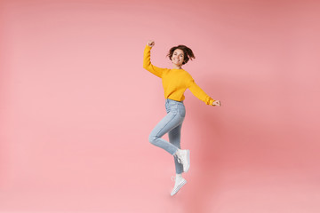 Fototapeta na wymiar Joyful young brunette woman girl in yellow sweater posing isolated on pastel pink wall background. People lifestyle concept. Mock up copy space. Having fun fooling around jumping doing winner gesture.