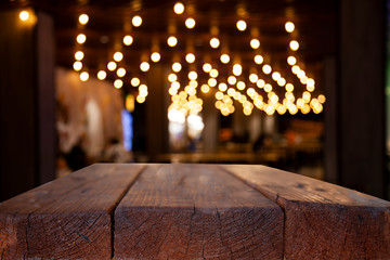 Empty wooden table top on blur light golden bokeh of cafe restaurant, bar in a dark background.