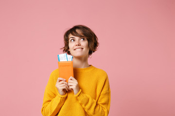 Pensive young brunette woman girl in yellow sweater posing isolated on pastel pink wall background. People lifestyle concept. Mock up copy space. Holding passport boarding pass ticket, looking up.