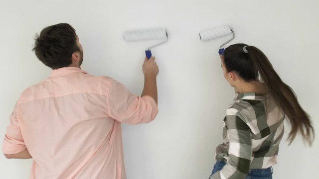 Positive young family painting wall in new home, laughing and dancing together