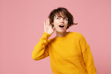 Curious young brunette woman girl in yellow sweater posing isolated on pastel pink wall background,...