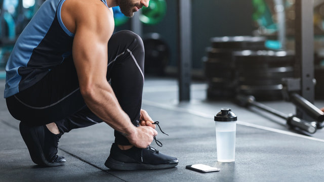 Athlete tying shoelaces on sneakers at gym, panorama