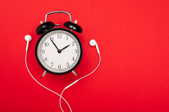 Minimalism Concept. Alarm Clock With Headphones On A Red Background With Copy Space