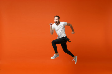 Fototapeta na wymiar Cheerful funny young man in casual white t-shirt posing isolated on bright orange wall background studio portrait. People lifestyle concept. Mock up copy space. Having fun, fooling around, jumping.