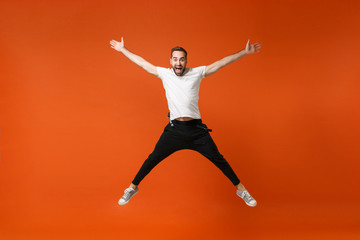 Fototapeta na wymiar Joyful young man in casual white t-shirt posing isolated on orange background studio portrait. People sincere emotions lifestyle concept. Mock up copy space. Have fun jumping spreading hands and legs.