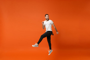 Fototapeta na wymiar Cheerful funny young man in casual white t-shirt posing isolated on bright orange wall background studio portrait. People lifestyle concept. Mock up copy space. Having fun, fooling around, jumping.
