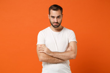 Serious young man in casual white t-shirt posing isolated on bright orange wall background, studio...