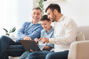 Father And Grandfather Teaching Boy Use Laptop Sitting On Couch