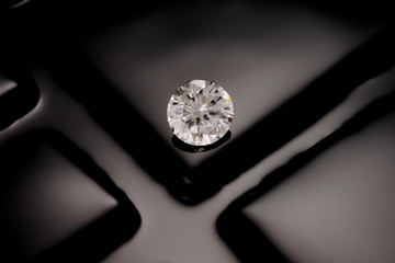 A solitaire, clean, clear, faceted, round diamond sits on a reflective background of black of fuse...