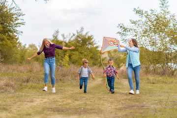 Happy non traditional family of two young mother and their kids launch a kite on nature at sunset