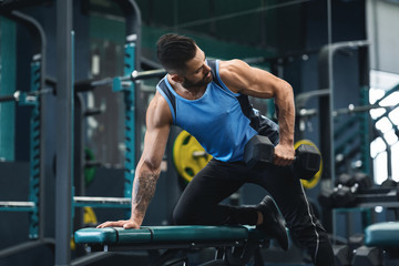 Fototapeta na wymiar Strong man training biceps with dumbbells at gym