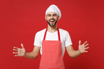 Cheerful young chef cook baker man in striped apron toque chefs hat posing isolated on red background. Cooking food concept. Mock up copy space. Gesturing demonstrating size with horizontal workspace.