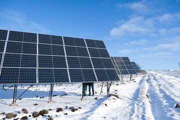 A series of solar panels in winter sunny morning on a snowy field in Ukraine. Fragment of two men's...