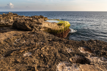 Rocky shoreline at Devil's Tear on island of Nusa Lembongan, Bali, Indonesia. Rocky shore with tidepool in foreground. Shoreline, ocean, sky & clouds in the background. 