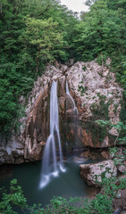 Fototapeta na wymiar A high waterfall falls from a cliff into a clear lake