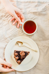 Fototapeta na wymiar Piece of Dark Chocolate Cake with Chocolate Glaze for Holiday and cup of tea. Top view. Sweet breakfast. Young woman hands. Process of eating