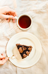 Piece of Dark Chocolate Cake with Chocolate Glaze for Holiday and cup of coffee. Top view. Sweet breakfast. Young woman hands. Process of eating
