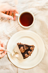 Piece of Dark Chocolate Cake with Chocolate Glaze for Holiday and cup of coffee. Top view. Sweet breakfast. Young woman hands. Process of eating