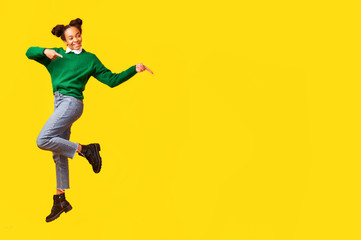 Happy afro teen jumping over yellow background and point