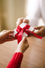 Man gives to his woman a gift box with red ribbon. Hands of man gives surprise gift box for girl. Young loving couple celebrating Valentine's Day.  Relationship, surprise, Birthday concept.