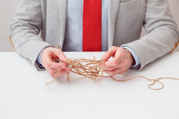 Alone businessman try to unwinds tangled thread ball like puzzle out situation. Conceptual photo.