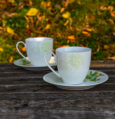 Two cups of tea stand on a wooden surface, against the background of autumn leaves.