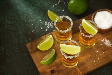 Mexican Gold Tequila shot with lime and salt on dark stone background. Copy space.