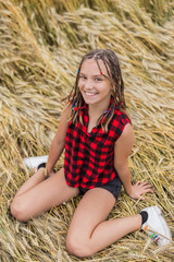 Naklejka na ściany i meble Smiling teenage girl with braids sitting in wheat field at summer