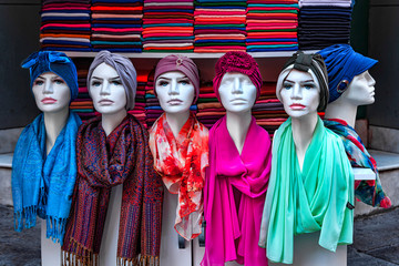 View of six mannequins from their waist to head, covered with colorful scarves and headscarves, as seen in a shop window in Istanbul Turkey. In the background even more scarves folded in colorful pile