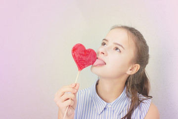 Young cute girl laughs, eating a heart shaped lollipop