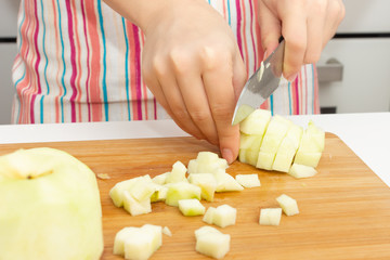 Making a cake. Girl cuts green apples with a knife in the kitchen