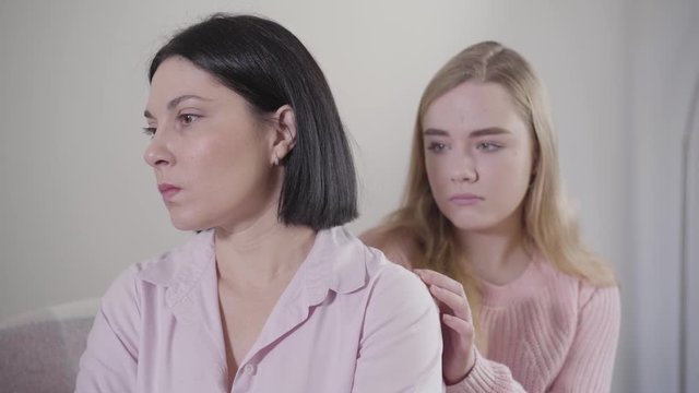 Portrait of blond Caucasian girl turning to mother and touching her shoulder. Teenage daughter making peace with mom after conflict. Family relationship, conflict, problems.