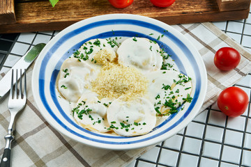 Close up view on homemade ravioli with meat with cream sauce, parmesan and herbs in a white ceramic plate on a white background. Tasty italian cuisine. Food flat lay