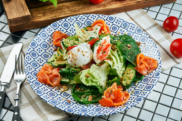 Close up view on appetizing salad with salmon, spinach, poached egg and ricotta in beautiful blue ceramic plate on white background. Tasty food. Flat lay