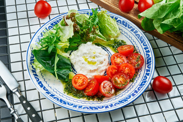 Close up view on appetizing salad with Italian strachatella cheese, lettuce, cherry tomatoes in beautiful blue ceramic plate on white background. Tasty food. Flat lay