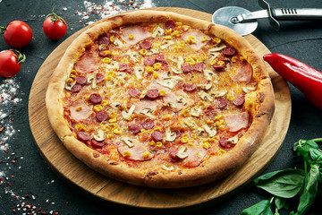 Pizza with a large number of toppings: hunting sausages, onions, mushrooms, salami, cheese and bell pepper. Pizza in composition with ingredients on a black background