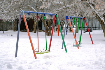 Children Playground with swings, in winter, covered with snow.