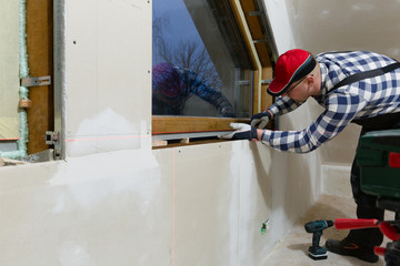 Handyman, construction man installing PVC window in a new insulated and filled dry wall attic.