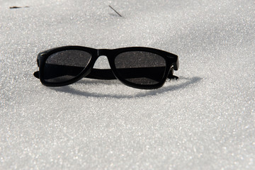 Polarized black sunglasses on white virgin snow, protect your eyesight