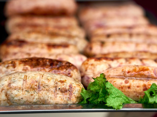 Rows of freshly grilled chicken meat sausages on tray with fresh lettuce at street food festival, selective focus, close-up. Unhealthy oily barbeque street fast food for meat lovers concept