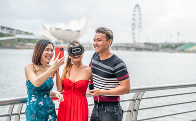 Three asian young friends outdoor wearing vr glasses and taking selfies. Happiness and holiday concept